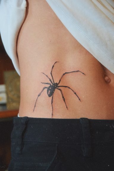 Tatouage d'une araignée noire sur le flanc d'une personne.