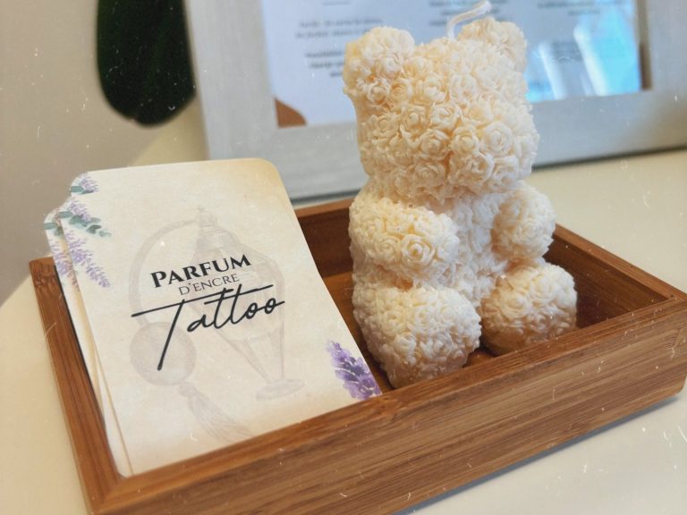 Ourson en peluche blanc à côté d'une carte "Parfum d'encre tattoo" dans un cadre en bois.