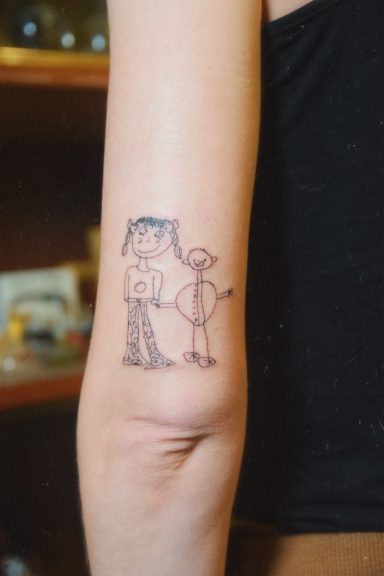 Tatouage représentant deux personnages de style dessin d'enfant sur un bras.