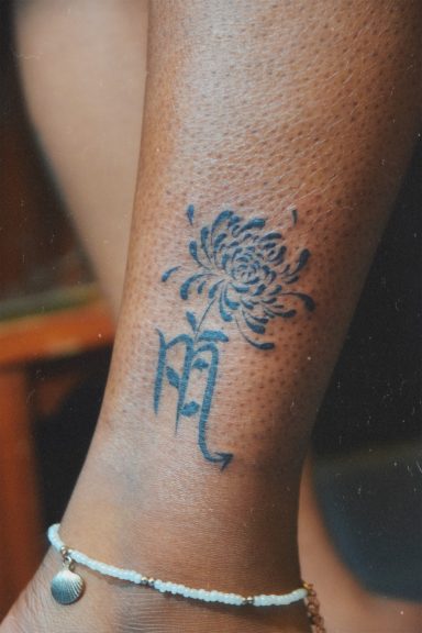 Tatouage d'une fleur stylisée avec le signe astrologique scorpion en dessous sur une cheville.