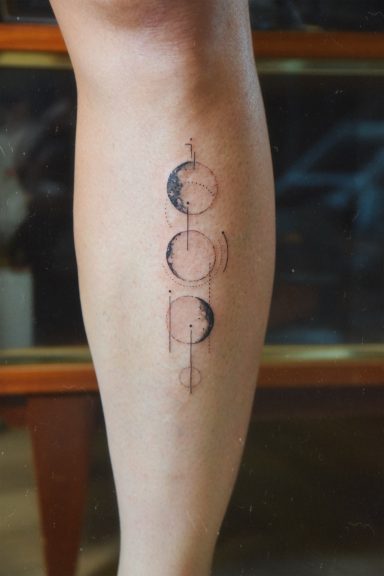 Tatouage sur un tibia représentant des phases de la lune en noir et blanc.