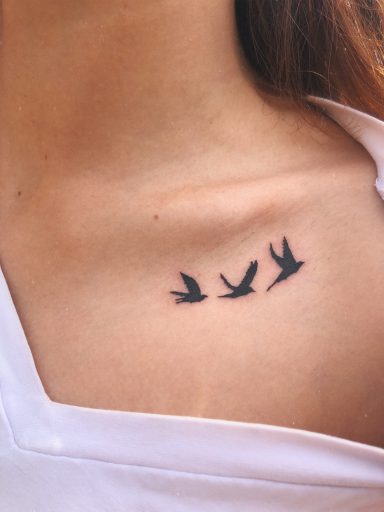 Trois oiseaux en vol, tatoués sur la peau près de la clavicule.